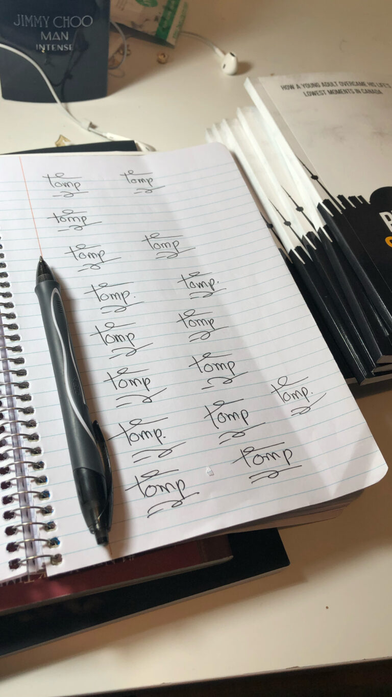 A spiral notebook filled with signature practice beside a pen and a stack of Pursuit of Success in a Foreign Land paperbacks