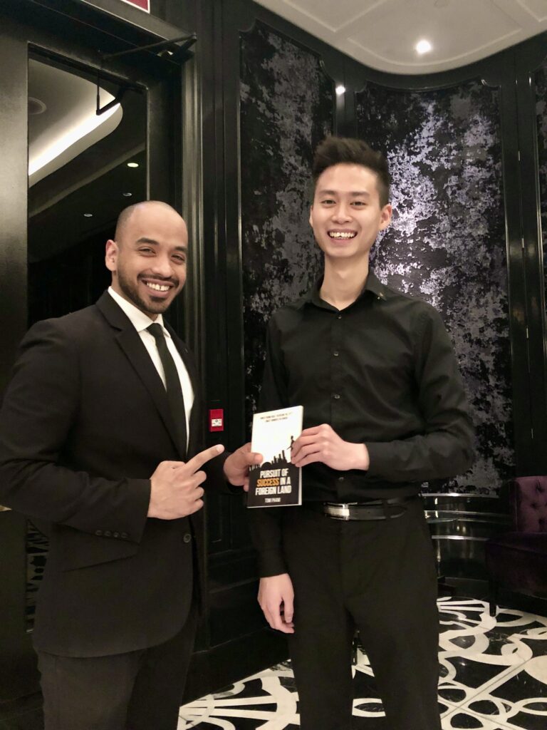 Tom and a friend at work smiling and holding the first book